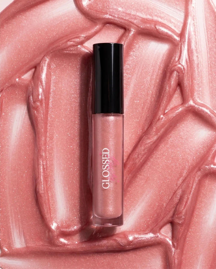 A Glossed by MJ lip gloss tube resting on a swirled bed of shimmering pink gloss.